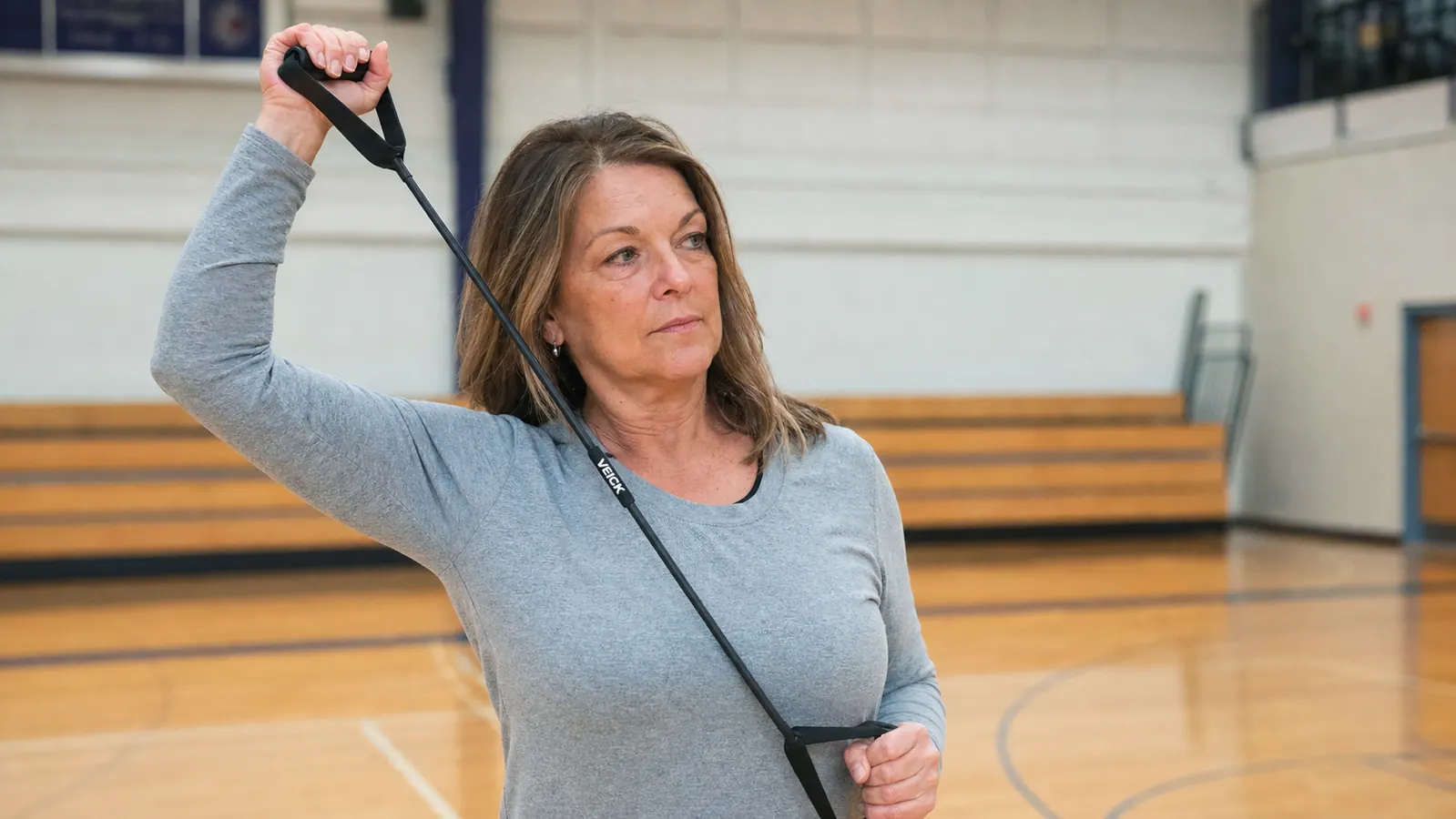A teenage volleyball player pulling a resistance band with handles overhead to loosen her shoulder before a match