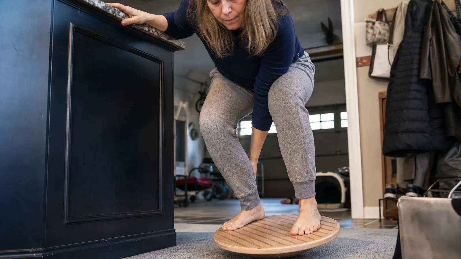 Close up of bare feet on the grip textured non slip surface of a wooden balance board, one hand steadying against a counter edge