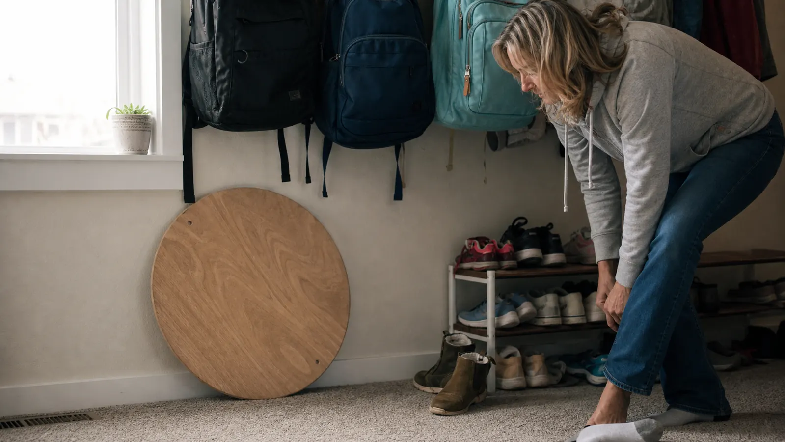 Wooden balance board leaning against the wall by a shoe rack near the front door instead of sitting in a closet