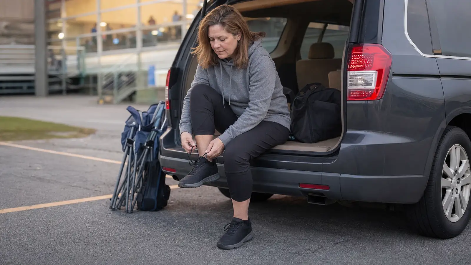 A teenage volleyball player sitting on a car tailgate lacing up sneakers after propping her feet up for a few minutes post tournament