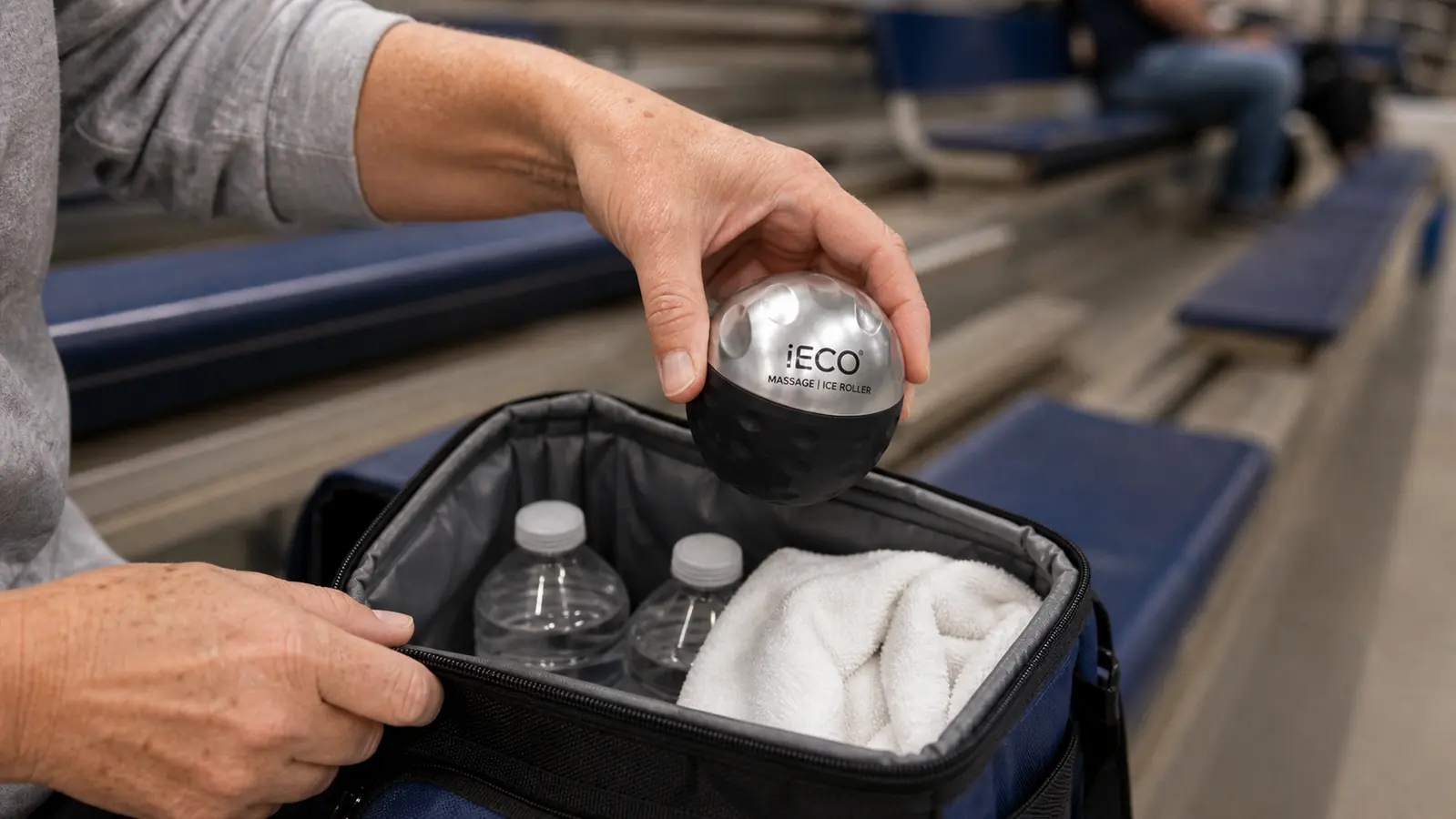A hand pulling the iECO ice roller out of a small cooler bag next to water bottles at a gym