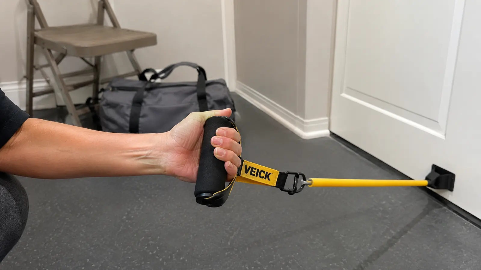 Hand gripping the molded handle of a VEICK resistance band looped through a door anchor for a shoulder warm up